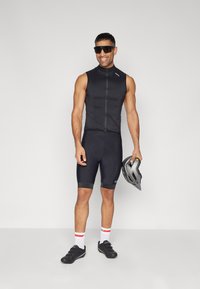 Completo da ciclismo nero con top senza maniche e pantaloni shorts imbottiti. Gli accessori includono occhiali da sole neri, scarpe nere e un casco grigio.