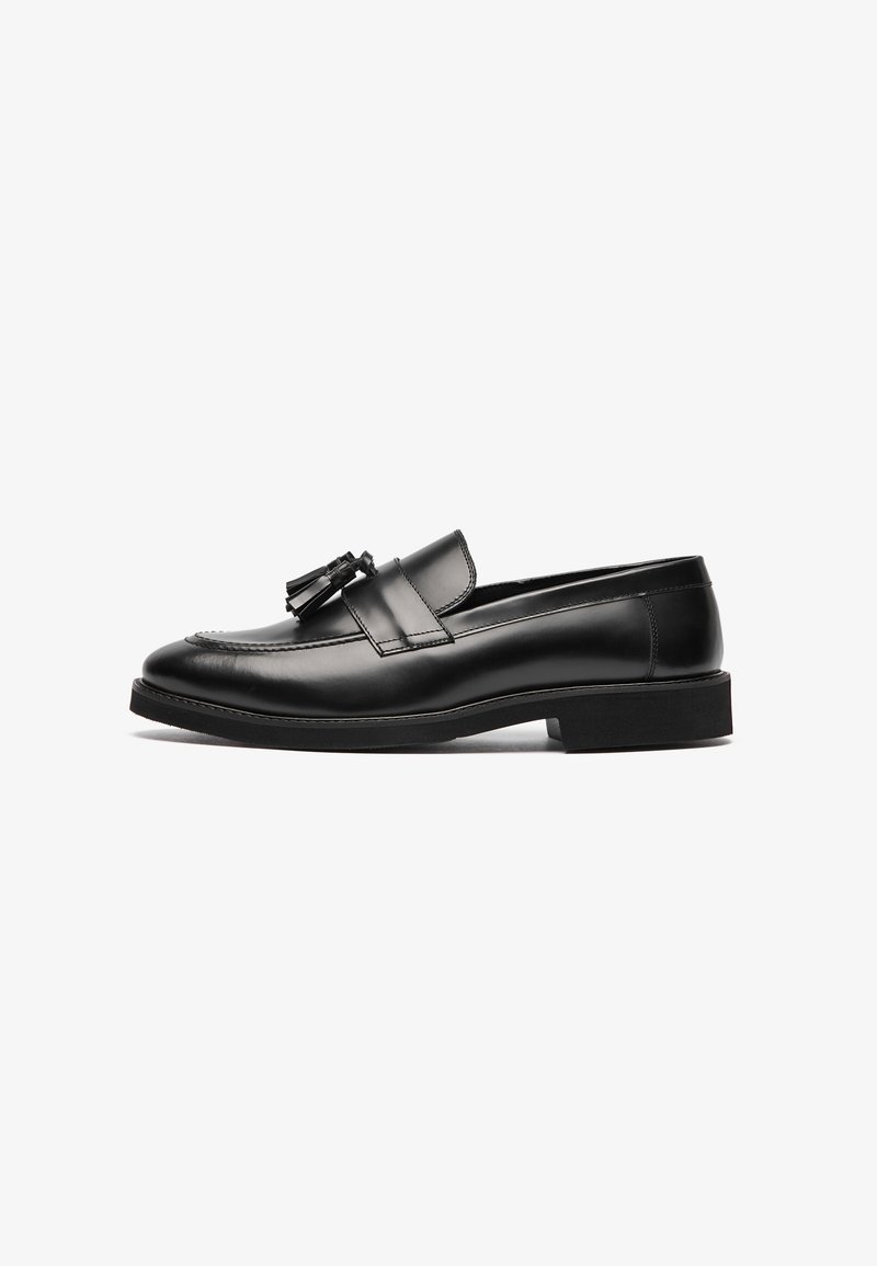 Mocassin en cuir noir avec pampilles, talon bas, bout arrondi et couture détaillée, présenté de profil sur fond blanc.