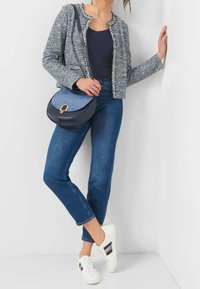 Blå tweedjacka med fransad fåll, marinblå linne, ljusblå axelremsväska, blå jeans och vita sneakers med röda och blå accenter.