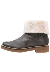 Bottine en cuir gris avec un revers en fausse fourrure blanche, bout arrondi, semelle épaisse marron et couture le long des côtés.