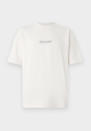 T-shirt bianco in cotone con collo rotondo e maniche corte, con un piccolo logo grigio "HOLLISTER" centrato sul petto.