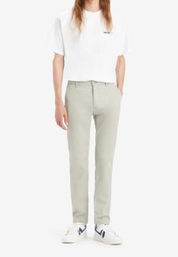 Jasnoszare bawełniane chinosy w połączeniu z białą koszulką Levi's, noszone z białymi trampkami z granatowymi akcentami. Luźny krój i design.