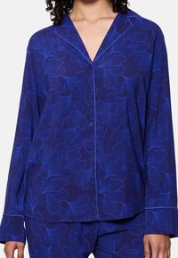 Donkerblauw pyjama bovenstuk met een bloemenpatroon in lichter blauw, voorzien van een notch kraag, knopen aan de voorkant en lange mouwen. Zachte stoftextuur.