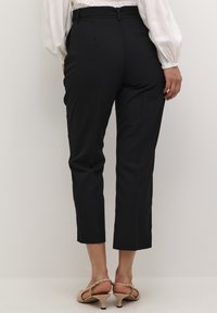 Čierne strihané nohavice so slim fit strihom, skrátenou dĺžkou a hladkým povrchom. Obsahujú pások na opasok a detail zadnej vrecka.