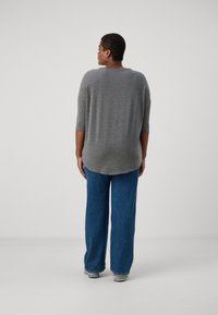 Gray, oversized sweater with a rounded hem and three-quarter sleeves, paired with loose blue denim jeans. Soft texture, casual fit.