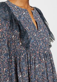 Robe bleu marine avec motif floral et oiseaux en rose, bleu et crème, dotée de volants en dentelle sur les épaules et d'un col en V.
