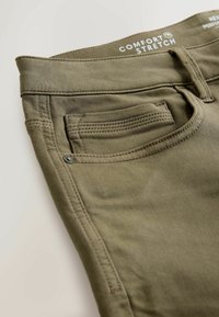 Olívové elastické nohavice s prednou kapsou, pútkami na opasok a viditeľnou nálepkou "Comfort Stretch" vo vnútri pásu.