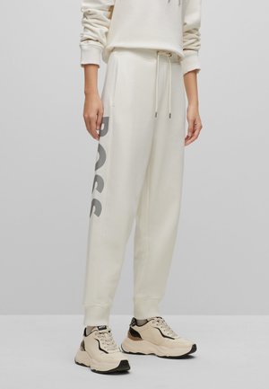 Persoon draagt off-white sweatpants met grote grijze tekst "BOSS" aan de zijkant en beige chunky sneakers met zwarte accenten.