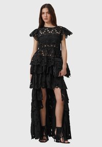 Black lace dress with layered design, short sleeves, and floral patterns. Paired with fringed black sandals and a textured clutch.