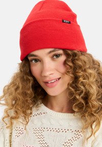 Rode geribbelde beanie met een omgeslagen ontwerp en een klein zwart "ROXY" label aan de zijkant. De gebreide textuur biedt warmte en comfort.