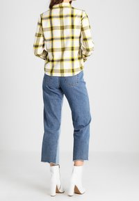 Camisa de franela a cuadros en blanco y amarillo combinada con jeans azules de cintura alta. Botines blancos con tacón grueso. Dobladillo de jeans deshilachado.