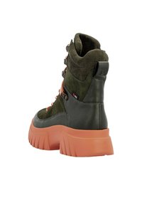 Botte imperméable verte avec semelle orange, empeigne texturée, col rembourré et quincaillerie en métal pour les lacets. Présente un design moderne et un talon épais.