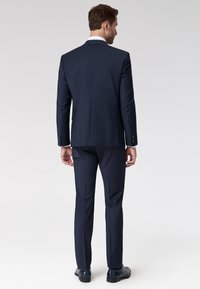 Marineblaues Sakko und passende Hose, strukturierte Passform, glattes Material, Gehschlitz hinten, elegante Schuhe, klare Linien, maßgeschneidertes Design.