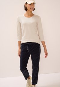 Ljusbeige långärmad topp med rund halsringning, tillsammans med mörkblå joggerbyxor med snörning och sidofickor. Neutrala sneakers.