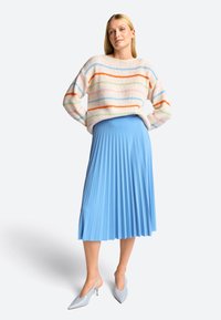 Mehrfarbig gestreifter Pullover aus weichem Strick; hellblauer plissierter Midirock; spitze hellblaue Slingback-Absätze.