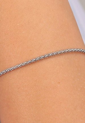 Silbernes Armband mit einer Reihe von kleinen, runden, klaren Kristallen, die in einem eleganten, dünnen Band eingefasst sind und auf einem hellen Hautton ruhen. Glatte Textur.