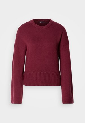 Burgundy neulepaita, jossa on pyöreä kaula-aukko, pitkät hihat ja ribbaushelma. Kangas näyttää pehmeältä ja teksturoidulta.
