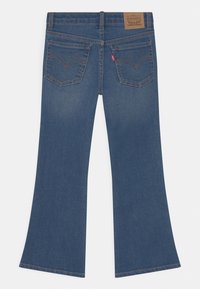 Jeans acampanados de mezclilla azul oscuro con cintura alta, dos bolsillos traseros con costuras distintivas y una etiqueta de cuero con la marca en la parte trasera.