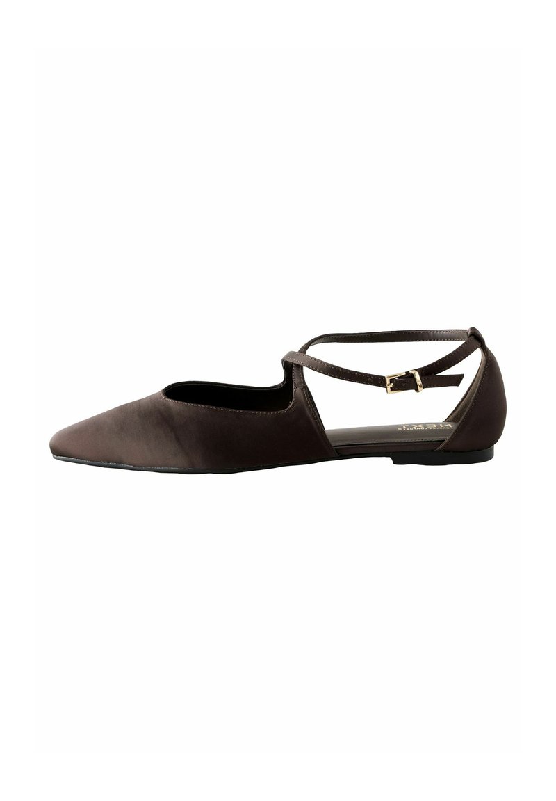Chaussures plates brunes avec un bout pointu, des côtés découpés, une sangle réglable et une texture douce. Présentent une semelle noire à faible hauteur.