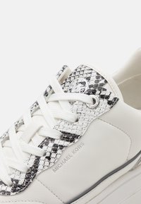 Sneaker bianca con accenti in pelle di serpente a fantasia nera e bianca. Presenta lacci bianchi piatti e un logo impresso sul lato.