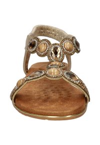 Gouden sandaal met een gestructureerde bruine voetbed, versierd met ronde en ovale edelstenen. Beschikt over twee banden en een elastische achterkant voor comfort.