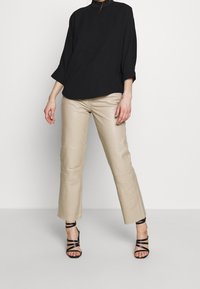 Svart oversized blus, krämfärgade byxor i konstläder med rak passform, och svarta strap-on klackar. Minimalistisk design, mjuk textur och neutrala färger.