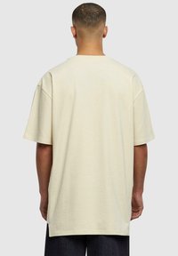 Tricou bej supradimensionat cu mâneci scurte �și tiv drept. Material moale și neted, cu cusături minime și fără grafice sau modele.