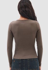 Långärmad topp i olivgrön ribbad väv. Har rundad hals, figurnära siluett och slät textur, kombinerad med denimjeans.