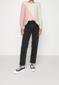 Stickad tröja med ett diagonalt mönster i rosa och krämfärg, som är matchad med högmidjade svarta jeans och svarta och vita lågt skurna sneakers.