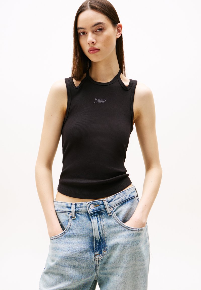 Black ribbed tank top with cut-out shoulder details and a small "tommy jeans" logo. Paired with light blue high-waisted jeans.