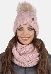Berretto in maglia rosa con un pom-pom morbido, caratterizzato da un motivo a treccia testurizzato. Abbinato a una sciarpa infinita in maglia rosa coordinata.