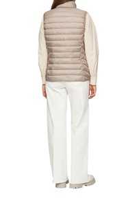 Beżowa pikowana kamizelka z poziomym wzorem, wysokim kołnierzem i lekką konstrukcją, zestawiona z kremowymi spodniami i miękkimi beżowymi butami.