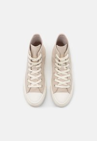 Beige vysoké tenisky vyrobené z hladké semišové látky, bílé tkaničky a bílý gumový špička. Obsahují jemný branding detail na boku.