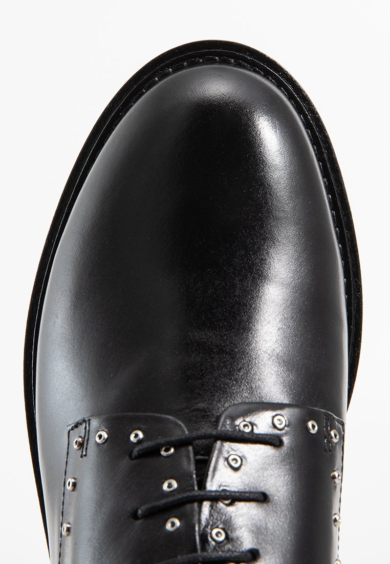 Chaussure habillée en cuir noir avec un bout poli, des lacets plats et des œillets en argent, possédant une texture lisse et une forme arrondie.