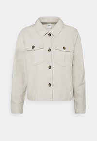 Beżowa krótka kurtka wykonana z bawełny, z kołnierzem, dwiema kieszeniami na piersi oraz pięcioma guzikami z przodu o matowym wykończeniu.