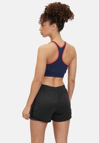 Sostenedor deportivo de malla en azul marino con detalles en rojo, diseño de tirantes cruzados. Combinado con pantalones cortos ligeros en negro que cuentan con una cinturilla elástica.