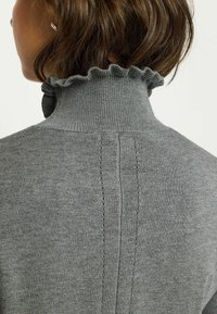 Maglione grigio con un collo alto e arricciato. Presenta cuciture verticali lungo la schiena e una texture liscia e morbida.