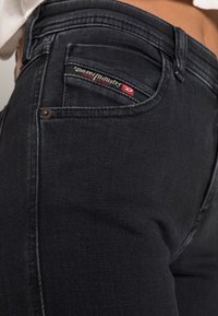 Close-up of black Diesel jeans showing side pocket with Diesel Industry Denim Division label and rivet detail.