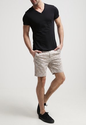 T-shirt noir à manches courtes et col en V associé à un short beige à motifs avec des tourbillons et des accents, porté avec des sneakers noires.