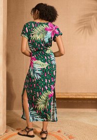 Žalia maxi suknelė, pagaminta iš audinio su daugiaspalviais gėlių ir leopardų raštais, su trumpomis rankovėmis ir šoninėmis skydelėmis, užtikrinančiomis patogumą judant.