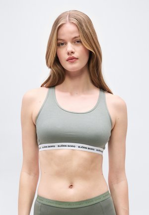 Γυναίκα με μακριά ξανθά μαλλιά, που φοράει αθλητικό μπουστάκι σε ανοιχτό πράσινο και αντίστοιχες κολάν με λογότυπα Björn Borg στις λάστιχες.