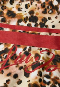 Tessuto con stampa leopardata con accenti rossastri e texture liscia. Include testo stilizzato in rosso, su uno sfondo beige smorzato.