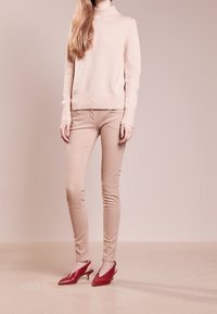 Svetle růžový pletený svetr s vysokým výstřihem, béžové skinny džíny a červené lodičky s jemným podpatkem. Hladké textury a jednoduchý design.