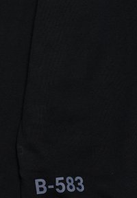 Tessuto nero con una trama liscia, caratterizzato dalla scritta stampata "B-583" in grigio, posizionata su un lato vicino all'orlo.