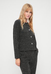 Μαύρο και άσπρο σακάκι από tweed με μακριά μανίκια, στρογγυλή λαιμόκοψη και τέσσερα έντονα κουμπιά. Συνδυασμένο με ταυτόσηπους παντελόνες. Λείο ύφασμα.