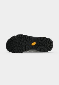 Semelle en caoutchouc noir avec des crampons profonds et un logo Vibram jaune au centre, vue de dessous.