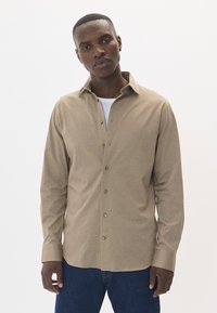 Bežinė ilgomis rankovėmis marškiniai su apykakle, užsegama mygtukais, tekstūruota medžiaga ir dviem priekinėmis kišenėmis. Yra žalvariniai mygtukai ir įprasto kirpimo dizainas.