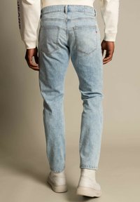 Jeans in denim azzurro chiaro a vestibilità slim, con tasche posteriori e una leggera scoloritura. Indossati con sneakers bianche alte.