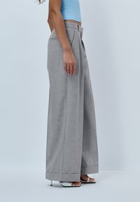 Gray wide-leg trousers with a tailored design, featuring a smooth texture and high waist, paired with open-toed white heels.