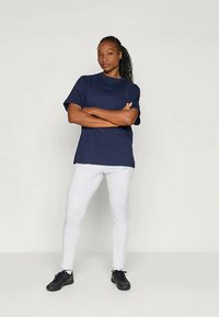 Navy blue short-sleeve t-shirt with a patterned logo, paired with white leggings and black athletic shoes, presented against a neutral background.